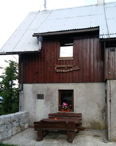 Napis na plošči: Partizanska kurirska postaja P-4 je bila ustanovljena marca 1943 v gozdu pod Skvarčem na Javorniku.